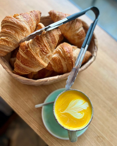 An image showing a tumeric latte and a basket of croissants at Emzi, a cafe in Clifton, Bristol