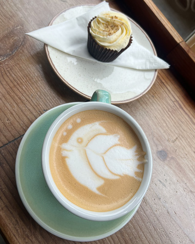 An image of a cupcake and a latte where the latte art looks like a fish at Emzi, a cafe in Clifton, Bristol