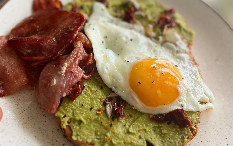An image showing a closeup of a meal containing avocado, bacon and fried eggs on toast. Served at Emzi, a cafe in Clifton, Bristol
