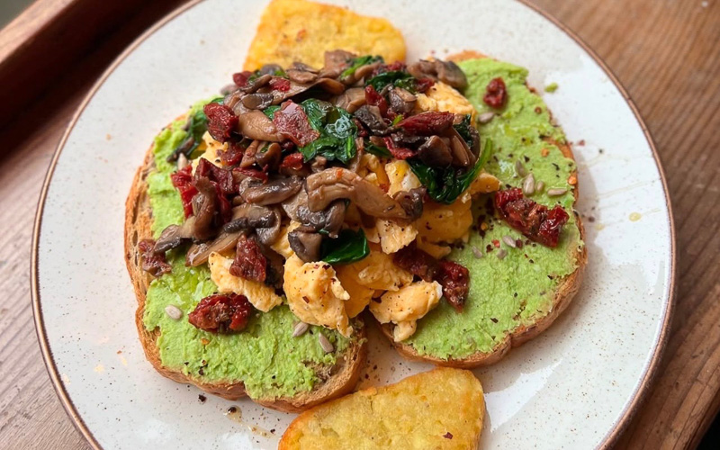 An image of a meal containing avocado, scrambled eggs, mushrooms and sundried tomatoes on toast. Served at Emzi, a cafe in Clifton, Bristol